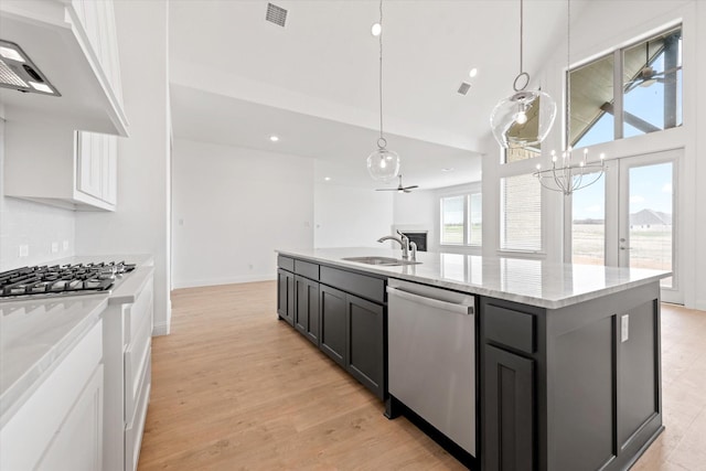 kitchen with stainless steel appliances, a center island with sink, ceiling fan with notable chandelier, white cabinets, and sink