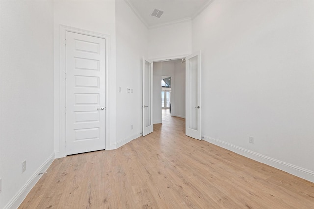 empty room featuring a towering ceiling, ornamental molding, and light hardwood / wood-style flooring