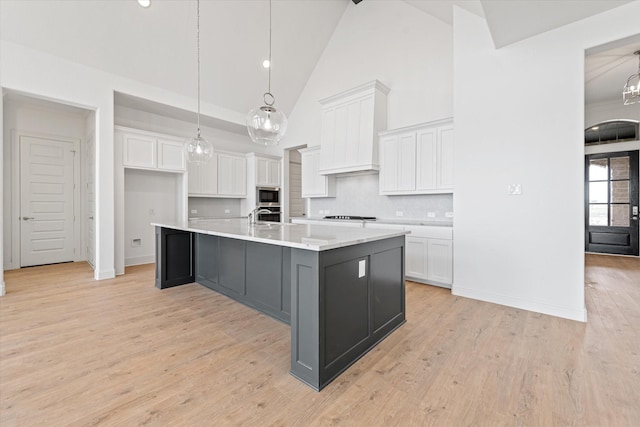 kitchen featuring an island with sink, stainless steel microwave, white cabinets, decorative light fixtures, and backsplash