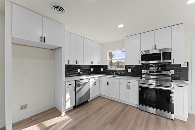 kitchen with sink, white cabinets, tasteful backsplash, light hardwood / wood-style flooring, and appliances with stainless steel finishes