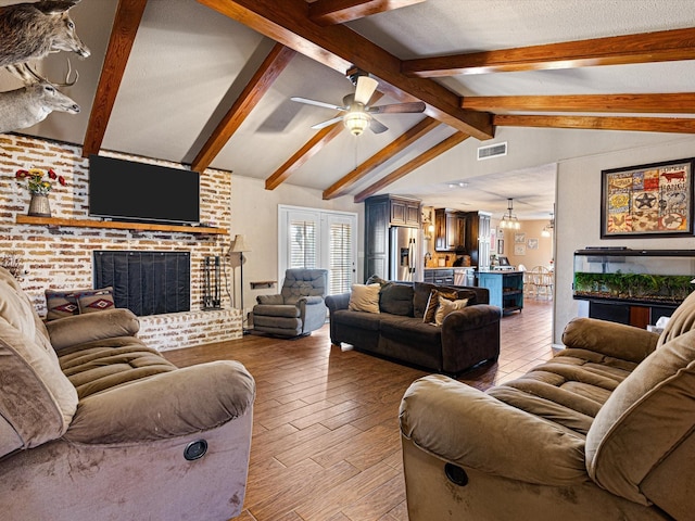 living room featuring ceiling fan with notable chandelier, a fireplace, and vaulted ceiling with beams