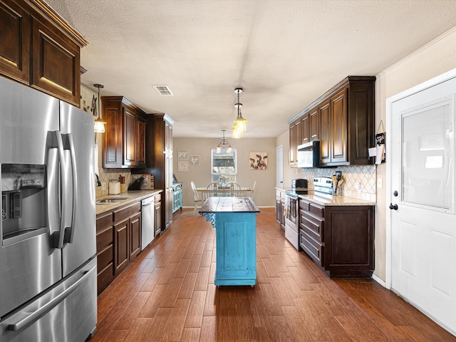 kitchen featuring hanging light fixtures, stainless steel appliances, a center island, and dark brown cabinetry