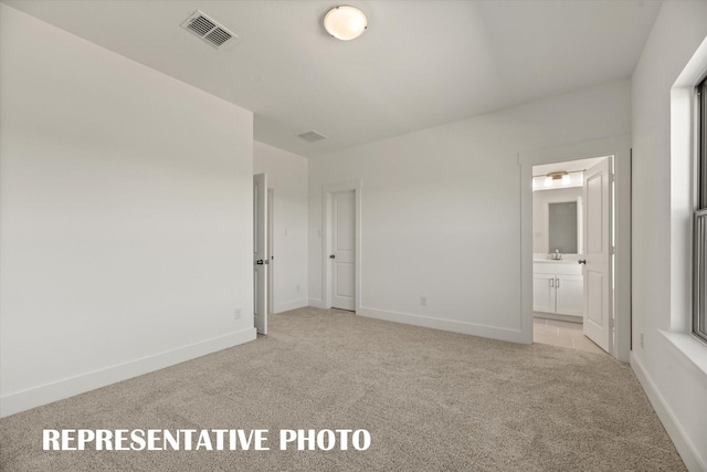 unfurnished bedroom with ensuite bathroom and light carpet