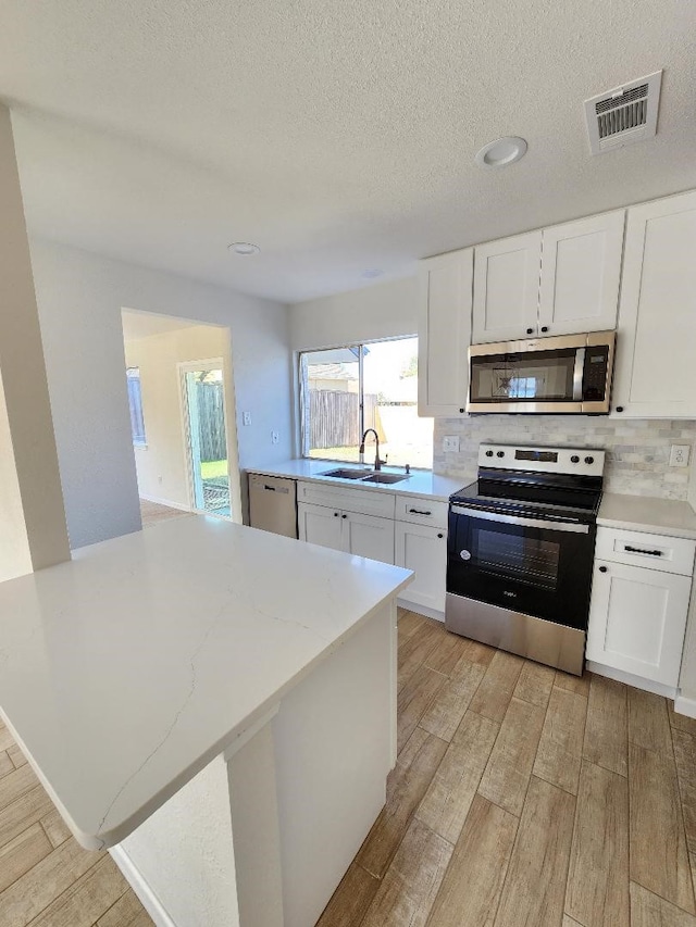 kitchen with stainless steel appliances, sink, white cabinets, light hardwood / wood-style floors, and backsplash