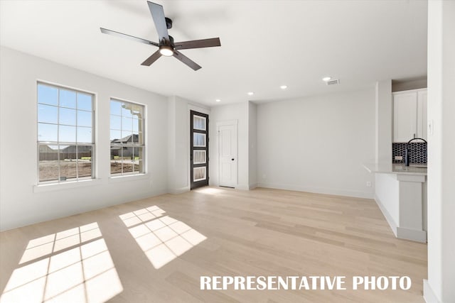 unfurnished living room with ceiling fan, light hardwood / wood-style flooring, and sink