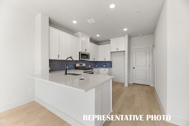 kitchen featuring white cabinetry, appliances with stainless steel finishes, kitchen peninsula, sink, and light hardwood / wood-style flooring