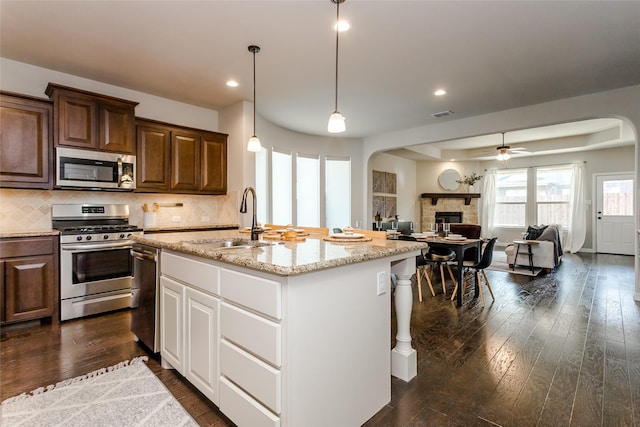 kitchen with sink, appliances with stainless steel finishes, decorative backsplash, a kitchen island with sink, and dark wood-type flooring