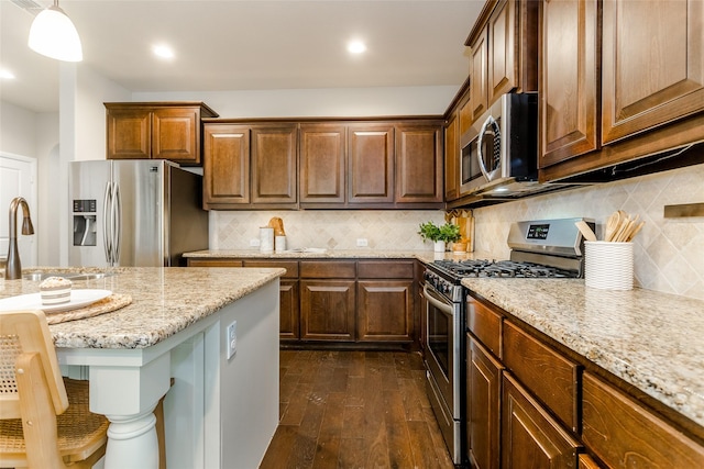 kitchen featuring stainless steel appliances, hanging light fixtures, dark hardwood / wood-style flooring, light stone counters, and sink