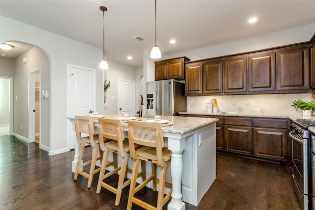 kitchen with stainless steel appliances, an island with sink, hanging light fixtures, light stone countertops, and decorative backsplash