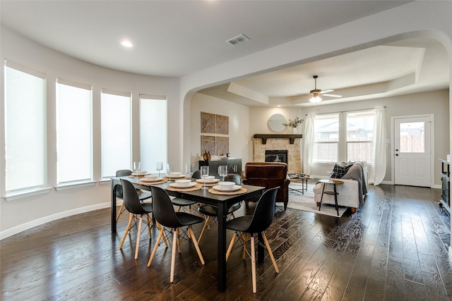 dining area featuring a fireplace, a tray ceiling, plenty of natural light, and dark wood-type flooring