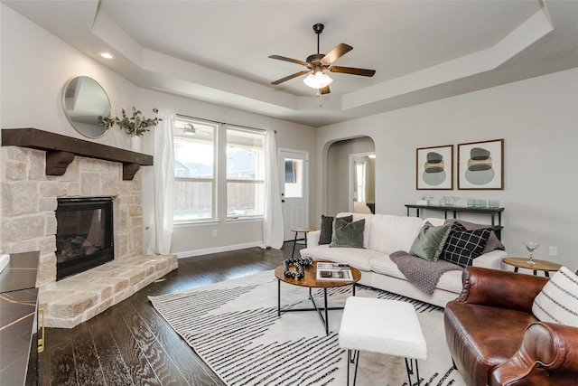 living room featuring a fireplace, ceiling fan, and a tray ceiling