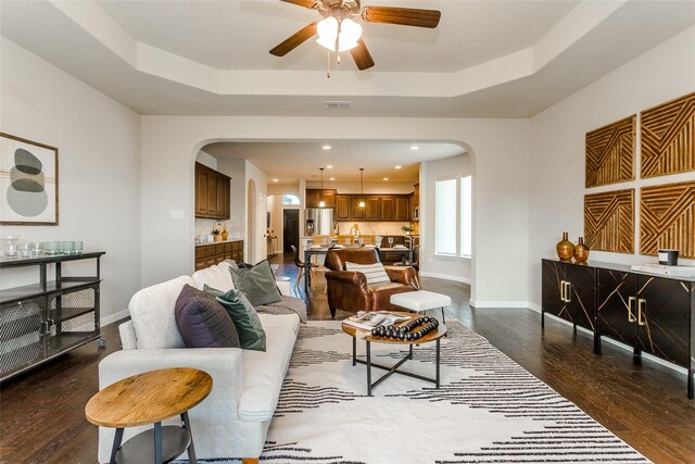 living room featuring dark wood-type flooring, a raised ceiling, and ceiling fan