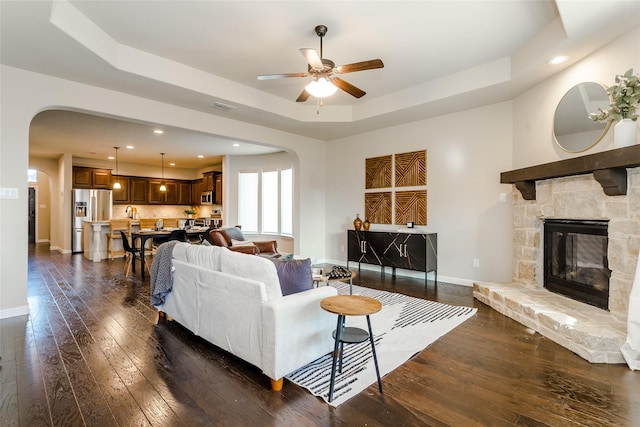 living room with a fireplace, ceiling fan, a tray ceiling, and dark hardwood / wood-style floors