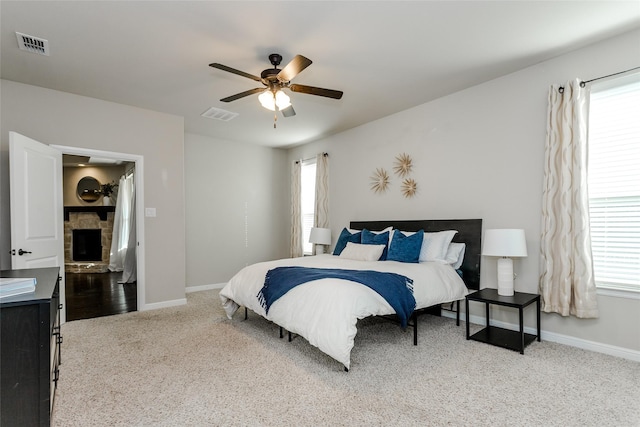 bedroom featuring a stone fireplace, ceiling fan, and carpet