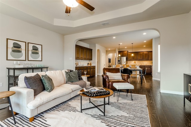 living room featuring ceiling fan, a raised ceiling, and dark hardwood / wood-style floors