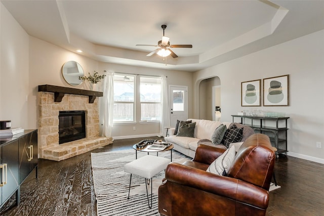 living room with dark hardwood / wood-style flooring, a fireplace, ceiling fan, and a tray ceiling