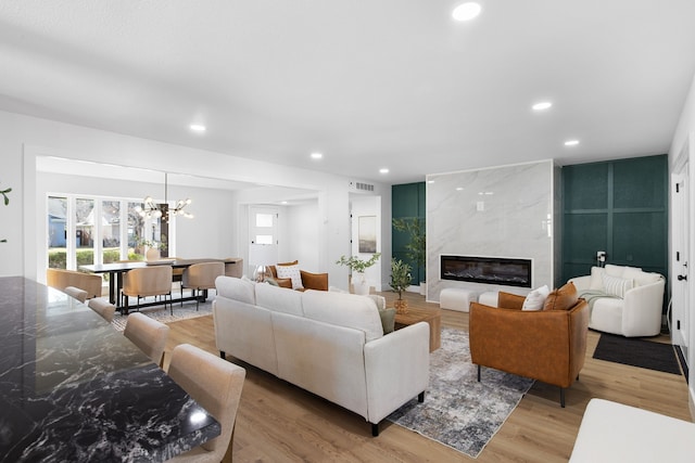 living room with a premium fireplace, light wood-type flooring, and a chandelier