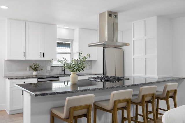 kitchen featuring stainless steel gas cooktop, white cabinetry, dark stone countertops, and island range hood