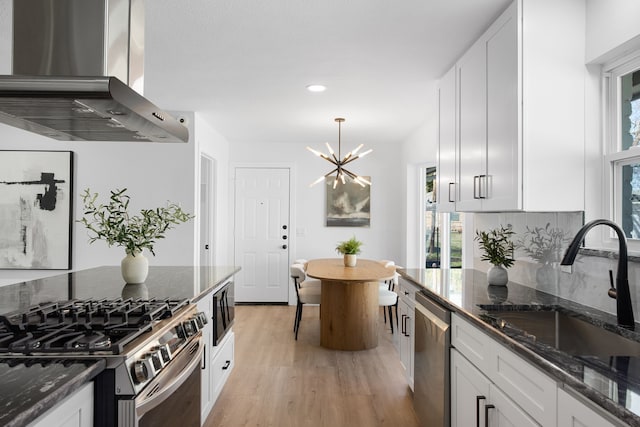 kitchen featuring island range hood, stainless steel appliances, dark stone counters, white cabinets, and sink