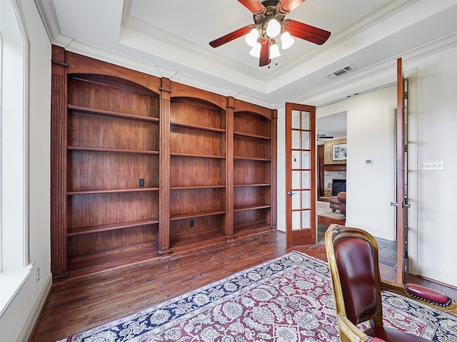 office space with ornamental molding, dark wood-type flooring, french doors, a tray ceiling, and built in shelves