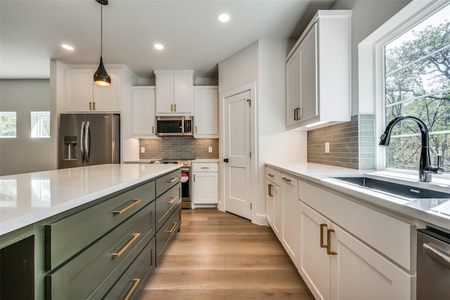 kitchen with appliances with stainless steel finishes, light hardwood / wood-style floors, white cabinets, decorative light fixtures, and sink