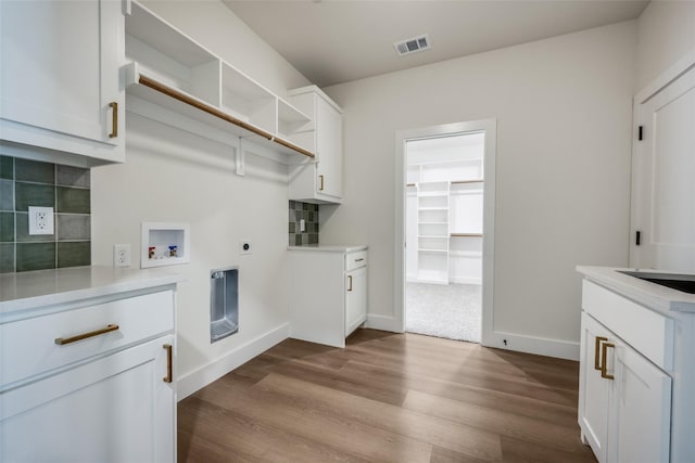 clothes washing area with electric dryer hookup, washer hookup, light wood-type flooring, and cabinets