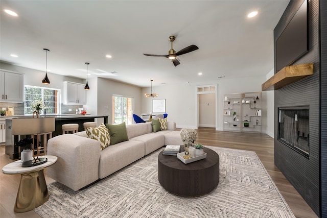 living room with ceiling fan with notable chandelier, a fireplace, and light wood-type flooring