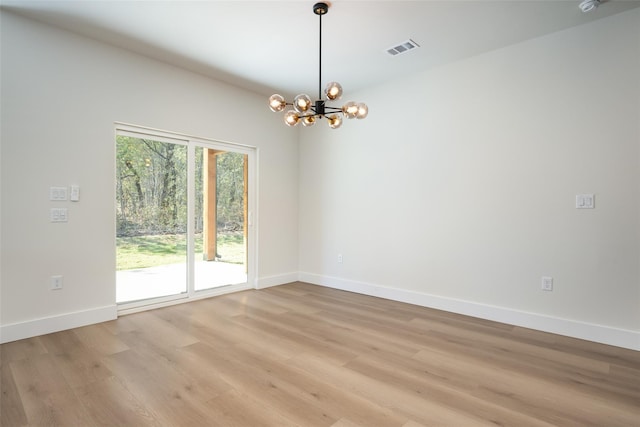 spare room featuring light wood-type flooring and a notable chandelier