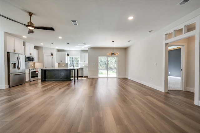 unfurnished living room featuring ceiling fan with notable chandelier and wood-type flooring