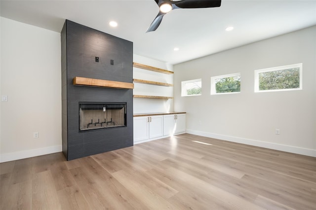 unfurnished living room with a large fireplace, ceiling fan, and light hardwood / wood-style flooring