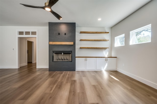 unfurnished living room with a large fireplace, ceiling fan, and light hardwood / wood-style flooring