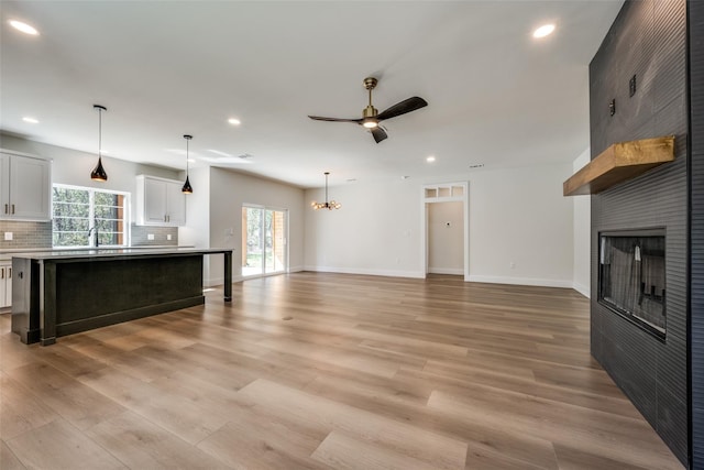 unfurnished living room with ceiling fan with notable chandelier, a fireplace, and light hardwood / wood-style floors