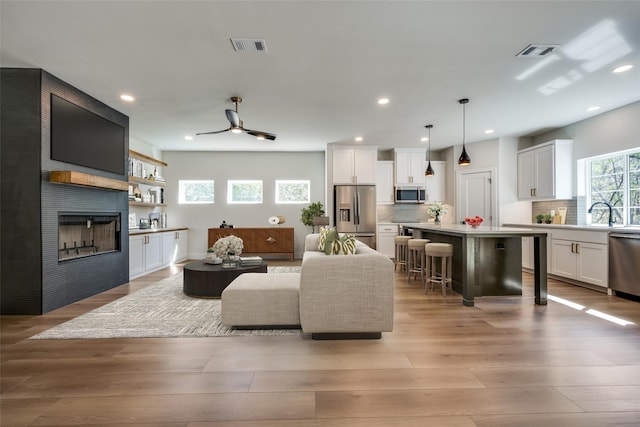 living room with ceiling fan, light wood-type flooring, sink, and a large fireplace