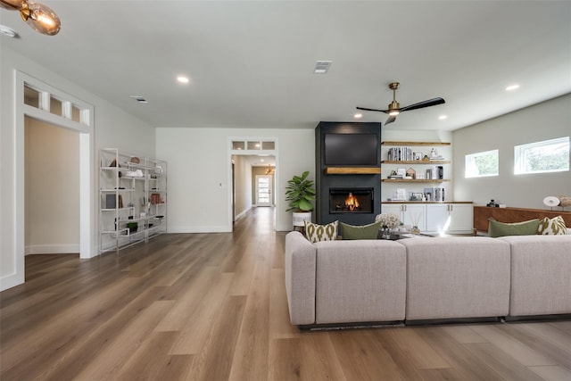 living room featuring a large fireplace, wood-type flooring, ceiling fan, and a healthy amount of sunlight