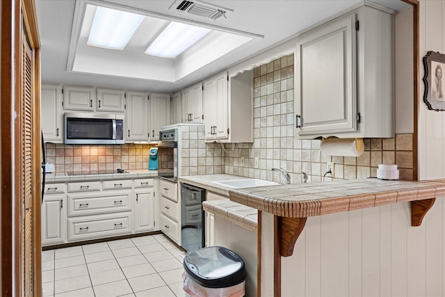 kitchen with a kitchen breakfast bar, tile counters, black appliances, kitchen peninsula, and white cabinetry