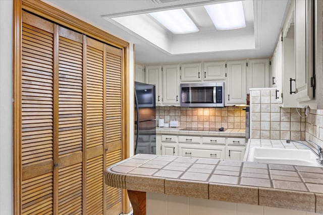 kitchen with tile countertops, black appliances, decorative backsplash, white cabinetry, and sink