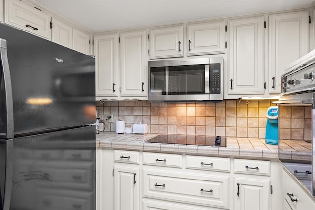 kitchen with tile countertops, black appliances, decorative backsplash, and white cabinetry