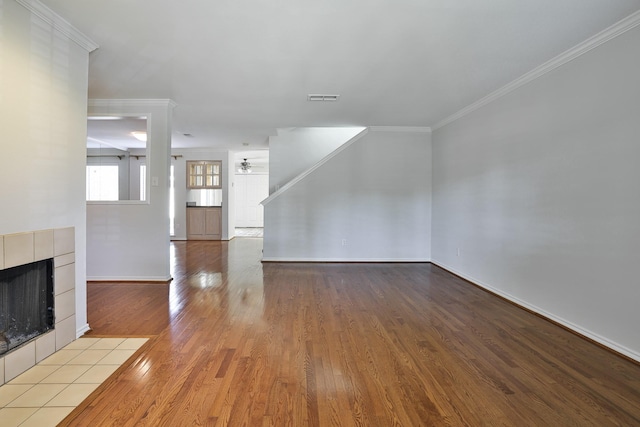 unfurnished living room featuring ceiling fan, light hardwood / wood-style flooring, a tile fireplace, and crown molding