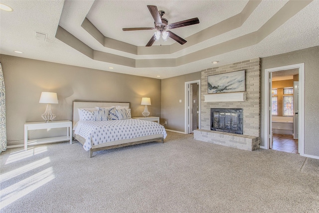 bedroom with carpet flooring, ceiling fan, a brick fireplace, ensuite bath, and a tray ceiling