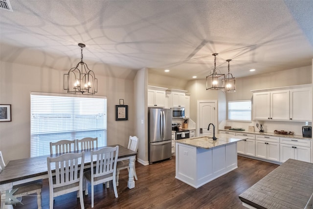 kitchen featuring appliances with stainless steel finishes, hanging light fixtures, light stone countertops, and a center island with sink