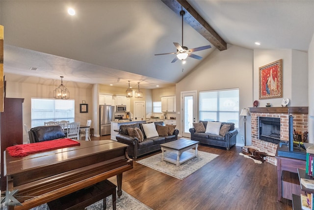 living room with ceiling fan with notable chandelier, a brick fireplace, high vaulted ceiling, beam ceiling, and dark wood-type flooring