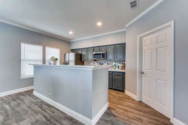 kitchen with appliances with stainless steel finishes, an island with sink, ornamental molding, and tasteful backsplash