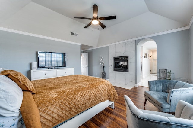 bedroom featuring vaulted ceiling, a tiled fireplace, ceiling fan, ornamental molding, and dark hardwood / wood-style flooring