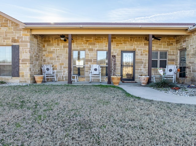 view of exterior entry with ceiling fan and a yard