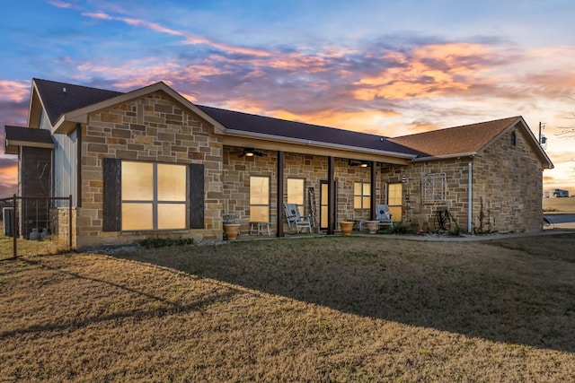 view of front of house featuring a ceiling fan, stone siding, and a yard