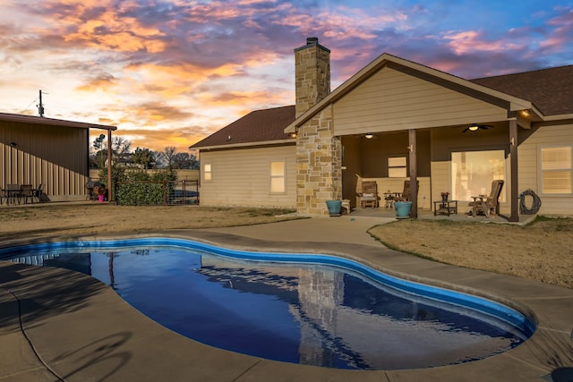 pool at dusk with ceiling fan and a patio area