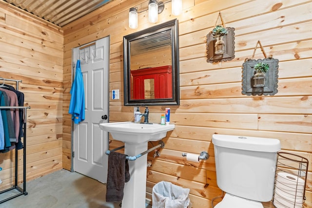 bathroom with wooden walls, concrete flooring, and toilet