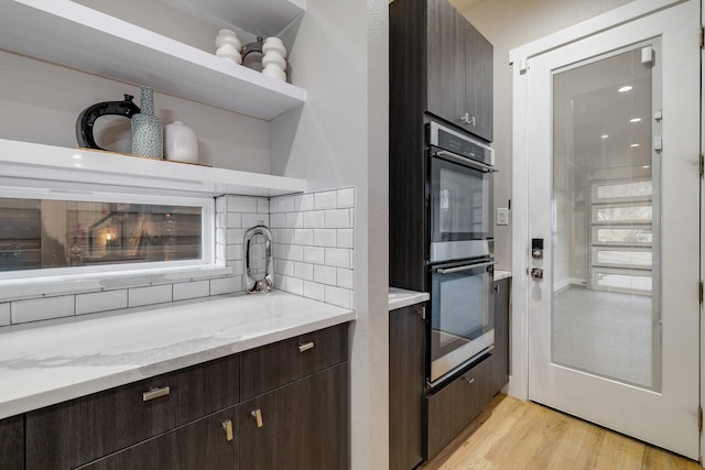 kitchen with light stone counters, backsplash, dark brown cabinets, and stainless steel double oven