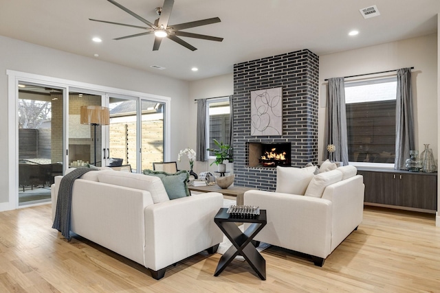 living room featuring a tile fireplace, ceiling fan, and light hardwood / wood-style flooring