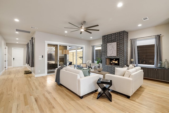 living room featuring light hardwood / wood-style flooring, a large fireplace, and ceiling fan